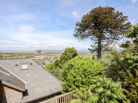 A rooftop with a chimney surrounded by trees and greenery with a distant view of fields and mountains at Bryn Awelon in Harlech