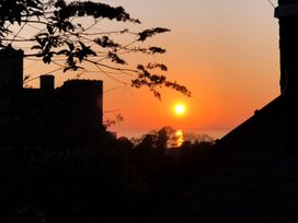 A sunset over water with silhouettes of trees a castle and a rooftop at Bryn Awelon in Harlech