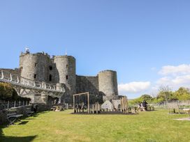 A playground with swings and benches near a stone castle at Bryn Awelon in Harlech