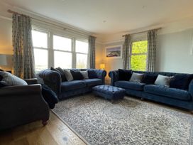 A living room with two blue sofas a matching ottoman a patterned rug and large windows at Bryn Awelon in Harlech
