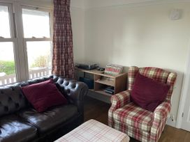 A living room with a brown leather sofa and plaid armchair with red pillows a wooden shelving unit with vinyl records and a turntable at Bryn Awelon in Harlech