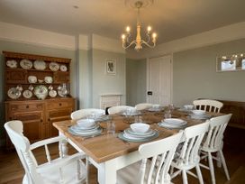 A dining room with a wooden table set for eight people white chairs a wooden cabinet with plates and cups on the wall and a chandelier at Bryn Awelon in Harlech