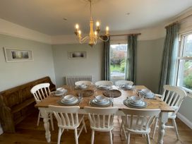 A dining room with a wooden table set for eight and white chairs at Bryn Awelon in Harlech