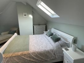 A bedroom with a bed, pillows, a blanket, a bedside table, a chair, and a chest of drawers at Bryn Awelon in Harlech