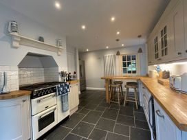 A kitchen with wooden countertops, white cabinets, a stove, two wooden stools at a breakfast bar, and a refrigerator at Bryn Awelon in Harlech