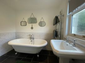 A bathroom with a bathtub, sink, mirrors on the wall and towels on a rail at Bryn Awelon in Harlech