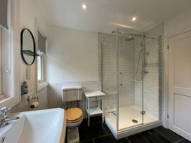 A bathroom with a sink, toilet with wooden seat, glass-enclosed shower, small white table, and a round mirror at Bryn Awelon in Harlech