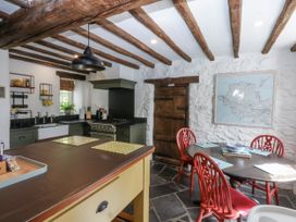 A kitchen with wooden beams, stove, and dining table at Tyddyn Iolyn in Benllech