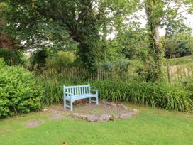 A garden with a bench surrounded by grass and trees at Tyddyn Iolyn in Benllech