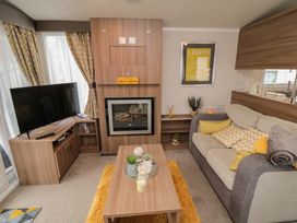 A living room with a sofa, a coffee table with plants and candles, a fireplace, a TV on a wooden stand, and curtains at Casa Cayton Beach in Scarborough