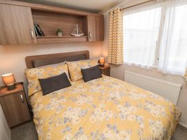 A bedroom with a double bed yellow floral bedding bedside tables lamps and a window with yellow patterned curtains at Casa Cayton Beach in Scarborough
