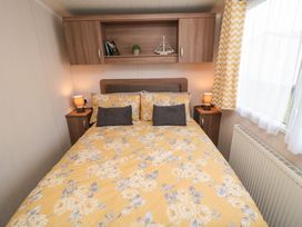 A bedroom with a bed with yellow floral bedding bedside tables lamps wall cabinets and a window with yellow patterned curtains at Casa Cayton Beach Scarborough