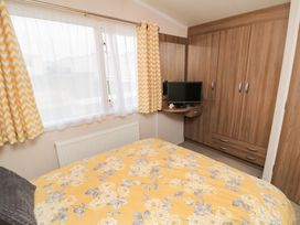 A bedroom with a bed covered in yellow floral bedding a window with yellow and white chevron curtains a wooden wardrobe and a small TV on a wooden shelf at Casa Cayton Beach in Scarborough