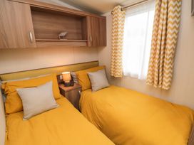 A bedroom with two single beds with yellow bedding and a nightstand with a lamp between them at Casa Cayton Beach in Scarborough