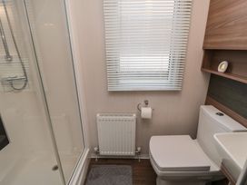 A bathroom with a shower enclosure a white toilet a window with blinds a radiator and a gray bath mat at Casa Cayton Beach in Scarborough