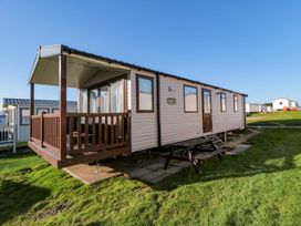 A mobile home with a wooden porch and picnic table on grass at Casa Cayton Beach Scarborough