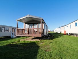 A mobile home with a wooden porch on grass with other mobile homes nearby at Casa Cayton Beach in Scarborough