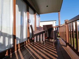 A wooden balcony with wicker chairs and a table outside sliding glass doors at Casa Cayton Beach in Scarborough