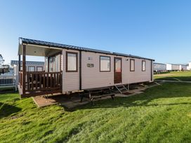 An exterior view of a beige and brown mobile home with a small porch and a picnic table on a grass lawn at Casa Cayton Beach in Scarborough