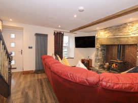 A living room with a red sofa a stone fireplace with wood burner and a wall-mounted TV at Miners Rest in Blaenau Ffestiniog
