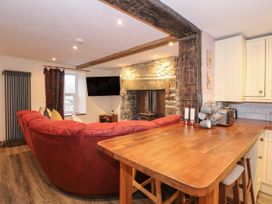 A living room with a red sectional sofa a mounted television a stone fireplace and a wooden kitchen counter with stools at Miners Rest in Blaenau Ffestiniog