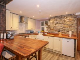 A kitchen with wooden countertops cream cabinets a stone feature wall and a small fridge at Miners Rest in Blaenau Ffestiniog