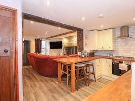 A kitchen with wooden countertops and stools next to a living room with a red sofa and stone fireplace at Miners Rest in Blaenau Ffestiniog