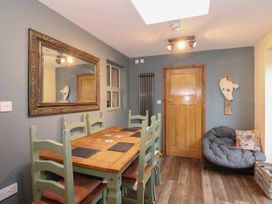A dining room with a wooden table and green chairs a large wall mirror a wooden door and a cushioned chair at Miners Rest in Blaenau Ffestiniog