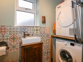 A laundry room with a sink on a wooden cabinet patterned tiles on the wall a washing machine and dryer stacked on a wooden shelf at Miners Rest in Blaenau Ffestiniog