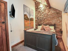 A bedroom with a dark wooden bed against a stone wall and two landscape paintings on a white wall at Miners Rest in Blaenau Ffestiniog