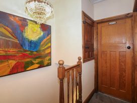 A hallway with wooden doors a colorful painting on the wall a chandelier and a wooden staircase railing at Miners Rest in Blaenau Ffestiniog