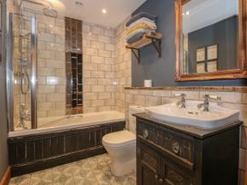 A bathroom with a bathtub shower combination a toilet a sink with a mirror above and towels on a wall shelf at Miners Rest in Blaenau Ffestiniog