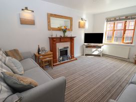 A living room with a striped carpet a grey sofa a wooden fireplace a TV on a cabinet and a window at Pebble Cottage in Whitby