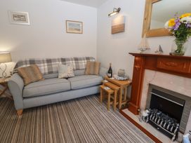 A living room with a gray sofa with cushions and a blanket a wooden fireplace with decorations and flowers on the mantel and a small nested table with a bottle and glasses at Pebble Cottage in Whitby