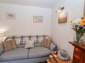 A sitting area with a gray sofa, cushions, a plaid blanket, framed pictures on the wall, a wooden table with a bottle and glasses, and a flower vase at Pebble Cottage in Whitby