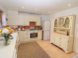 A kitchen with white cabinets a refrigerator a stove a microwave a wooden hutch and a vase of flowers on the counter at Pebble Cottage in Whitby