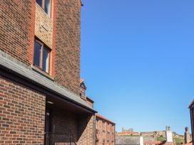 A view of brick buildings with a clear blue sky and ruins on a hill in the distance at Pebble Cottage in Whitby