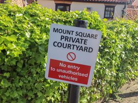 A sign reading Mount Square private courtyard no entry to unauthorised vehicles in front of green bushes and residential buildings