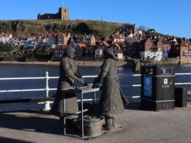Statues of two figures by the water with a trash bin at Pebble Cottage in Whitby