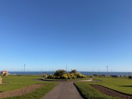 A pathway leading to a flower bed with the ocean in the background at Pebble Cottage in Whitby