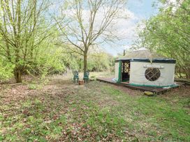 A yurt on a wooden platform surrounded by trees and green grass with two chairs and a tree stump in the clearing at Brandon House Farm Yurt Brandon Parva near Mattishall