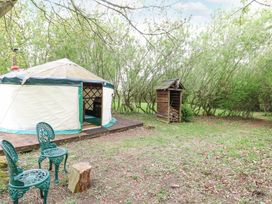 A yurt with two green chairs and wood storage in a wooded area at Brandon House Farm Yurt Brandon Parva near Mattishall