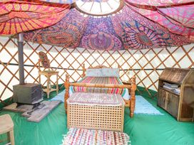 Interior of a yurt with a wooden bed, wood stove, chair with mirror, wooden storage cabinet, and colorful fabric ceiling at Brandon House Farm Yurt Brandon Parva near Mattishall