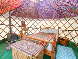 A wooden bed with striped bedding inside a yurt with a wood stove a wooden chair a nightstand with a lamp and patterned fabric on the ceiling at Brandon House Farm Yurt Brandon Parva near Mattishall