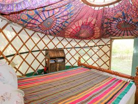 A bedroom inside a yurt with a wooden bed, striped bedding, wooden bookshelf, and patterned fabric ceiling at Brandon House Farm Yurt Brandon Parva near Mattishall