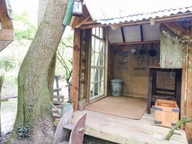 A small wooden outdoor shed with an open door showing hanging pans a metal bucket a wooden crate and a watering can at Brandon House Farm Yurt Brandon Parva near Mattishall