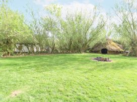 An outdoor area with grass fire pit trees wooden hut and yurt at Brandon House Farm Yurt Brandon Parva near Mattishall