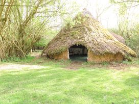 A grass field with a thatched hut surrounded by trees at Brandon House Farm Yurt in Brandon Parva near Mattishall