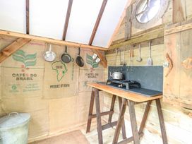 A rustic kitchen setup with hanging pans and utensils a kettle on a two-burner stove and coffee sacks on the wall at Brandon House Farm Yurt Brandon Parva near Mattishall