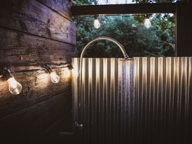 An outdoor shower with a metal corrugated wall wooden wall with string lights hanging at Brandon House Farm Yurt Brandon Parva near Mattishall